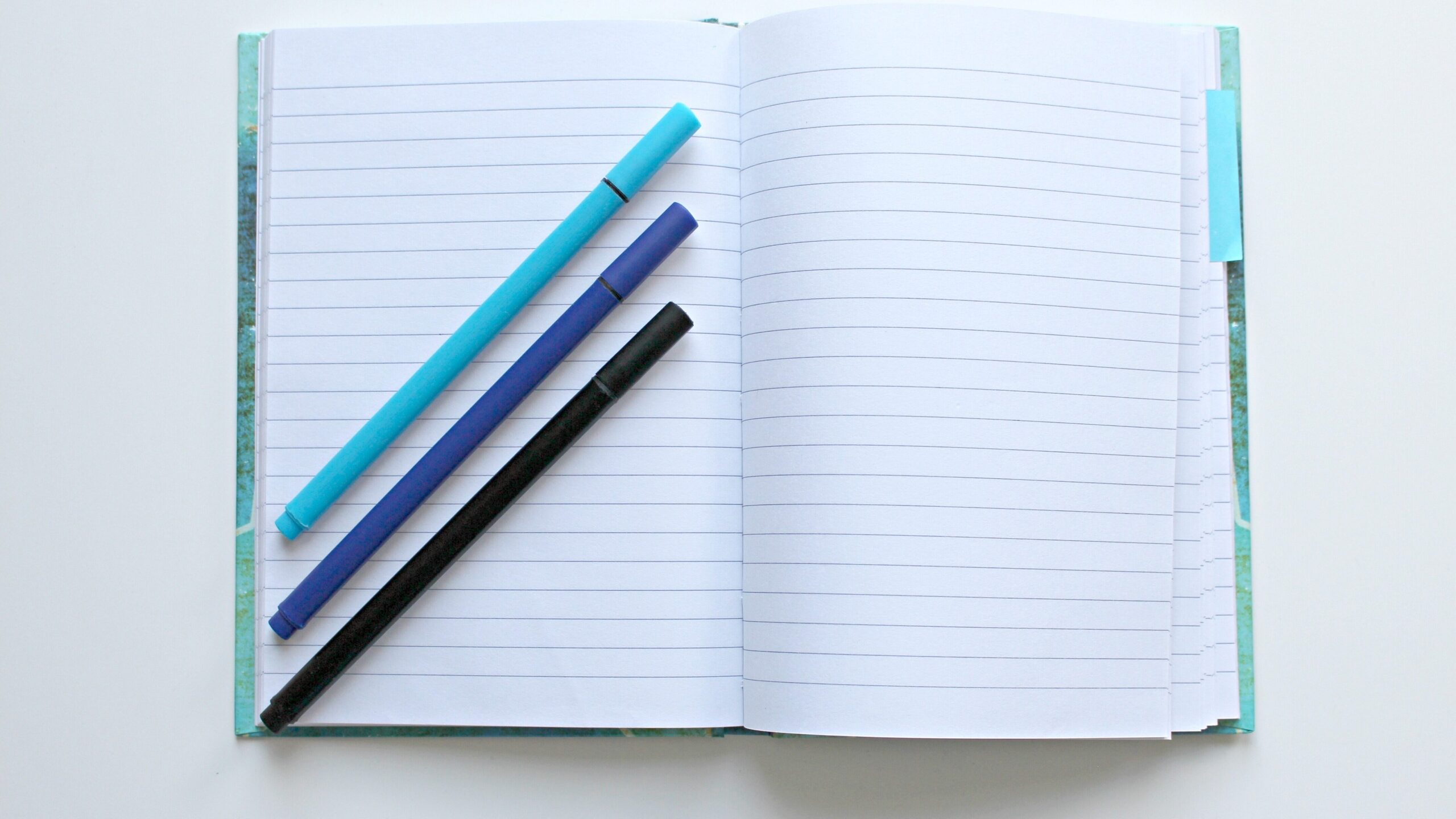 A lined notebook lies open with three pens on it, representing the beginning of a written story. 